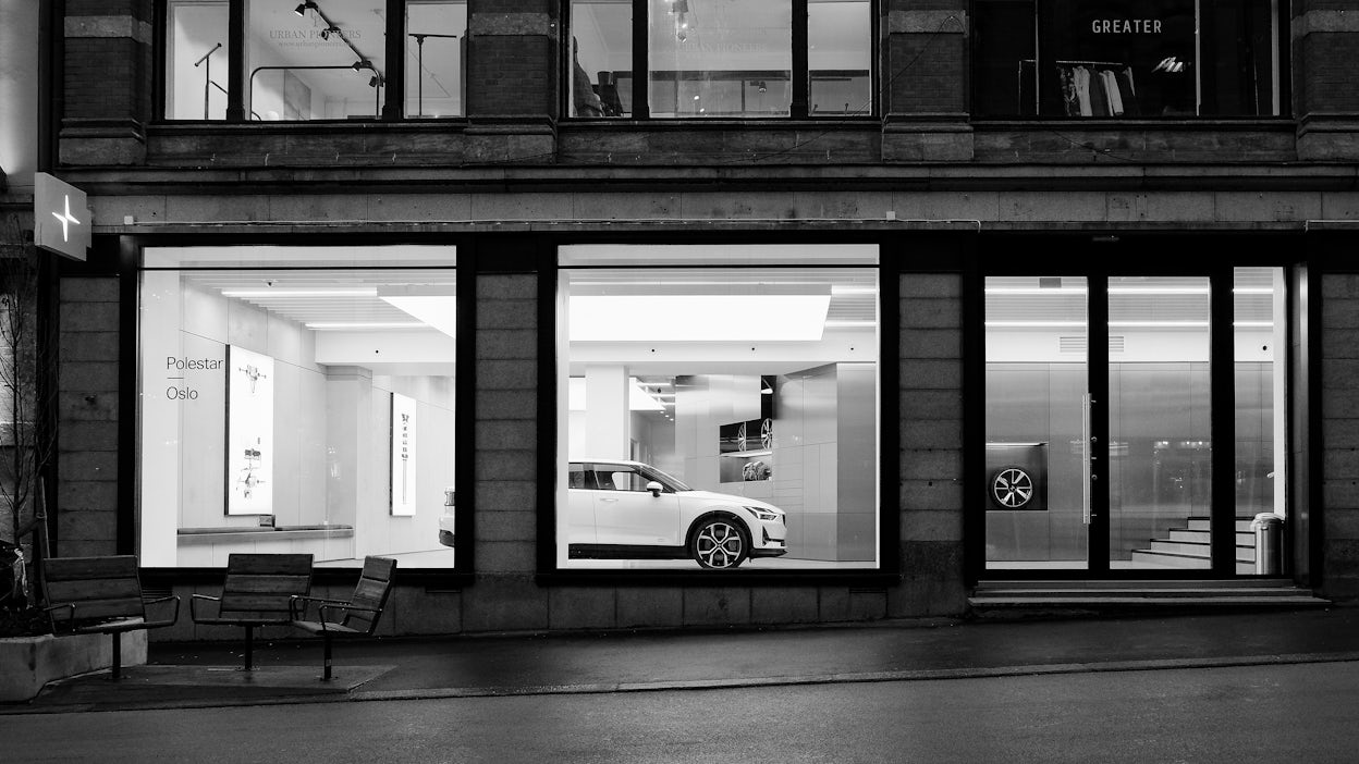 A street with a Polestar space, where a white Polestar is visible through the large glass windows.