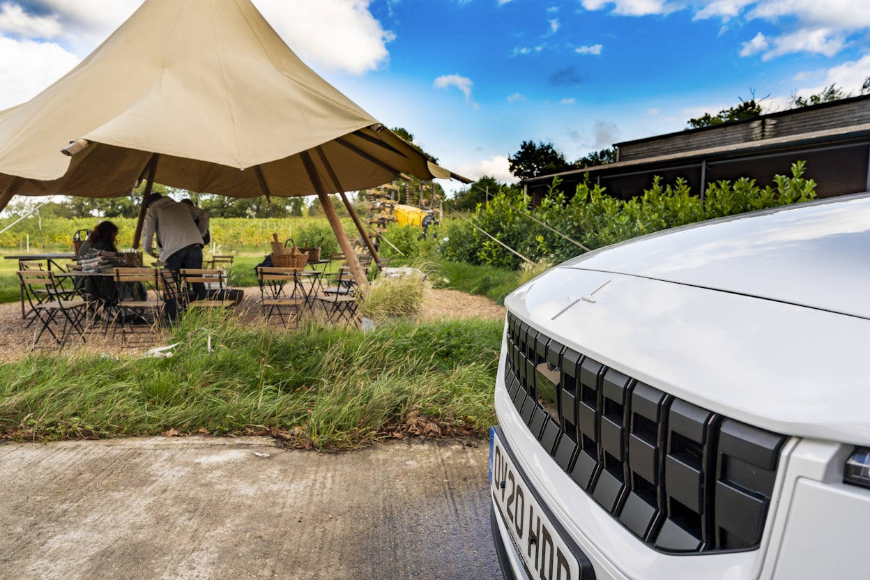 The front of a white Polestar 2 and a tent with tables and chairs visible in the background.