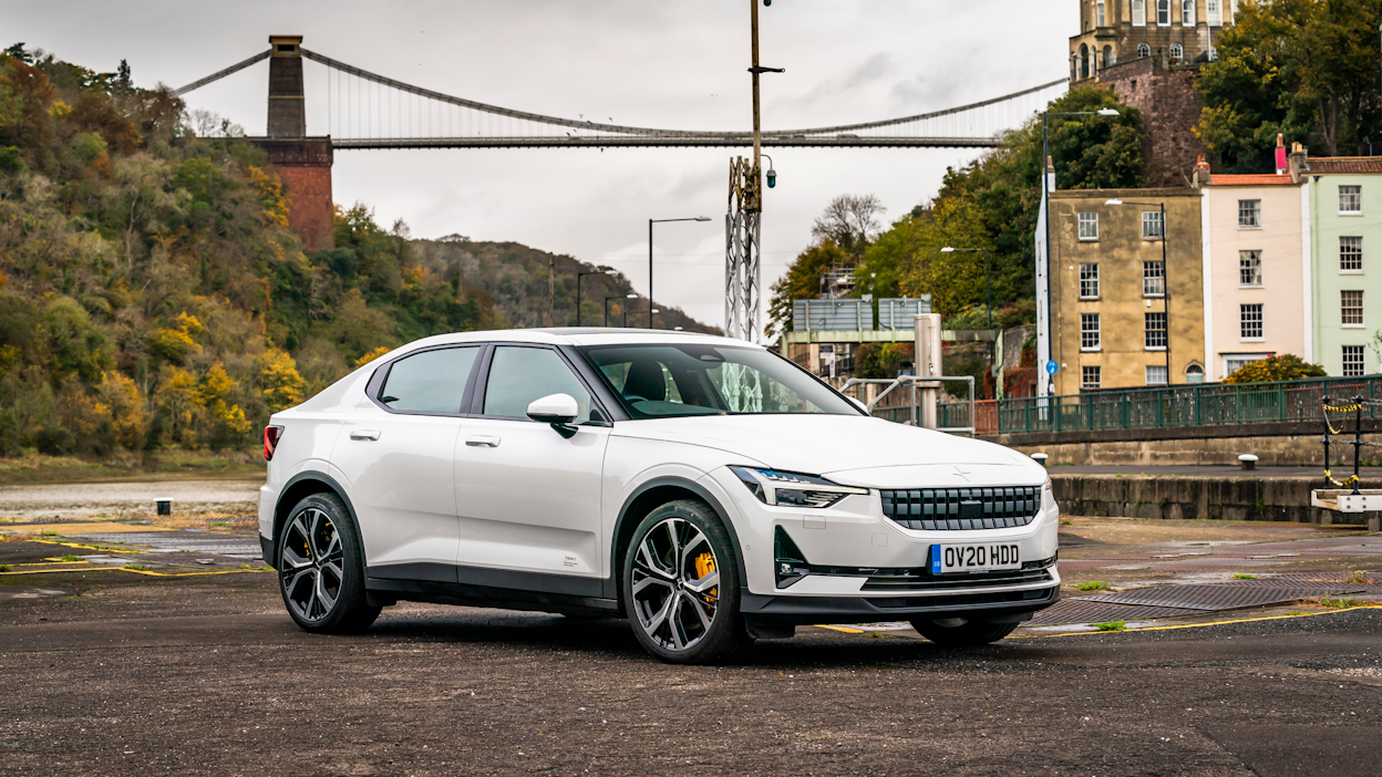 A white Polestar 2 parked on a empty parking lot in front of bridge.