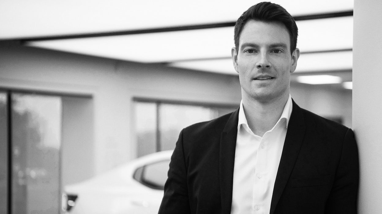 Black and white portrait of Alexander Lutz dressed in white shirt and dark suit jacket.