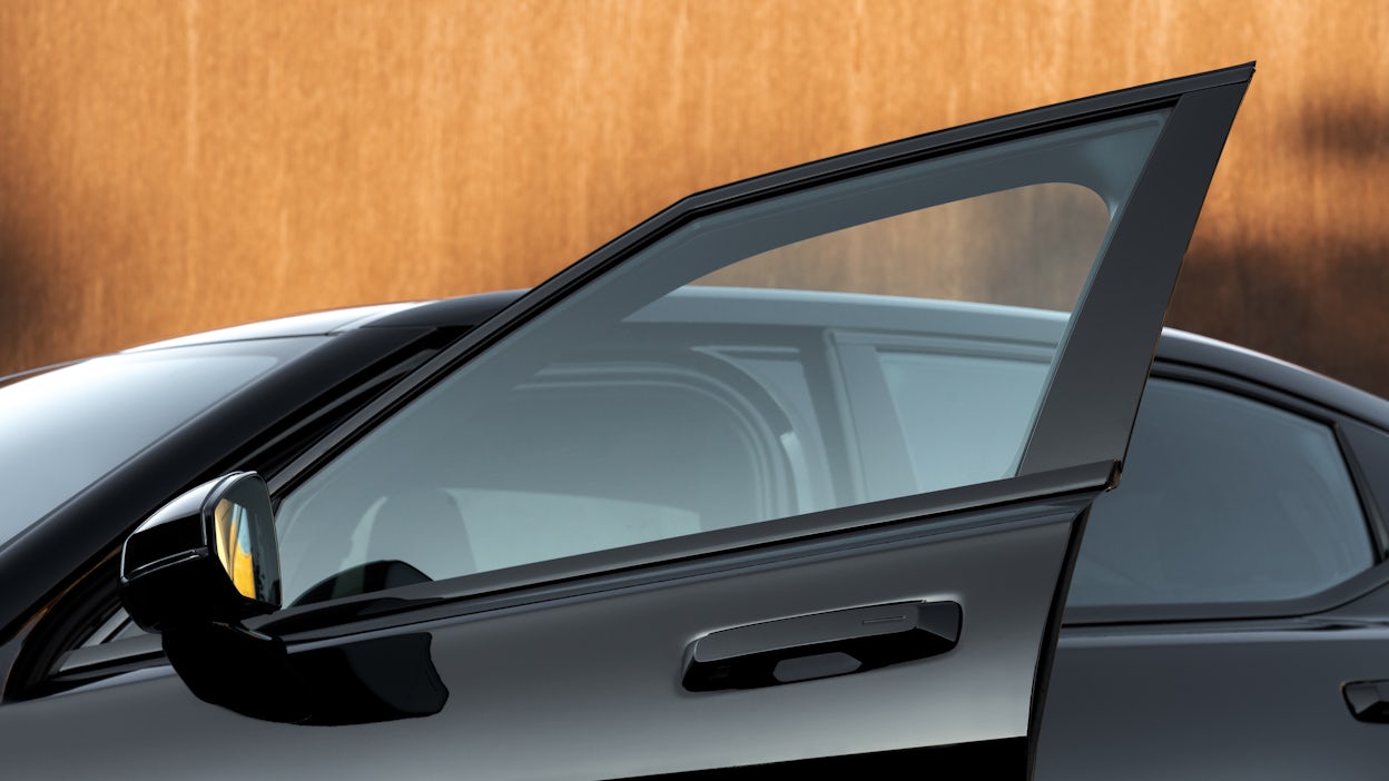 Black Polestar 2 in front of a wooden wall with focus on the open passenger door.