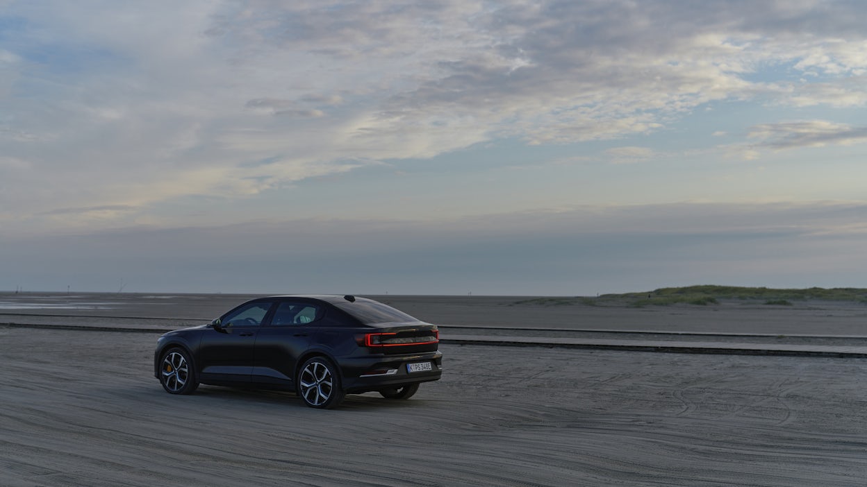 Black Polestar 2 driving on a beach.