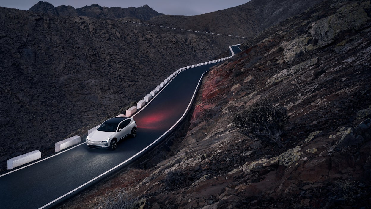 A white Polestar 2 driving on the road between mountains at dusk.