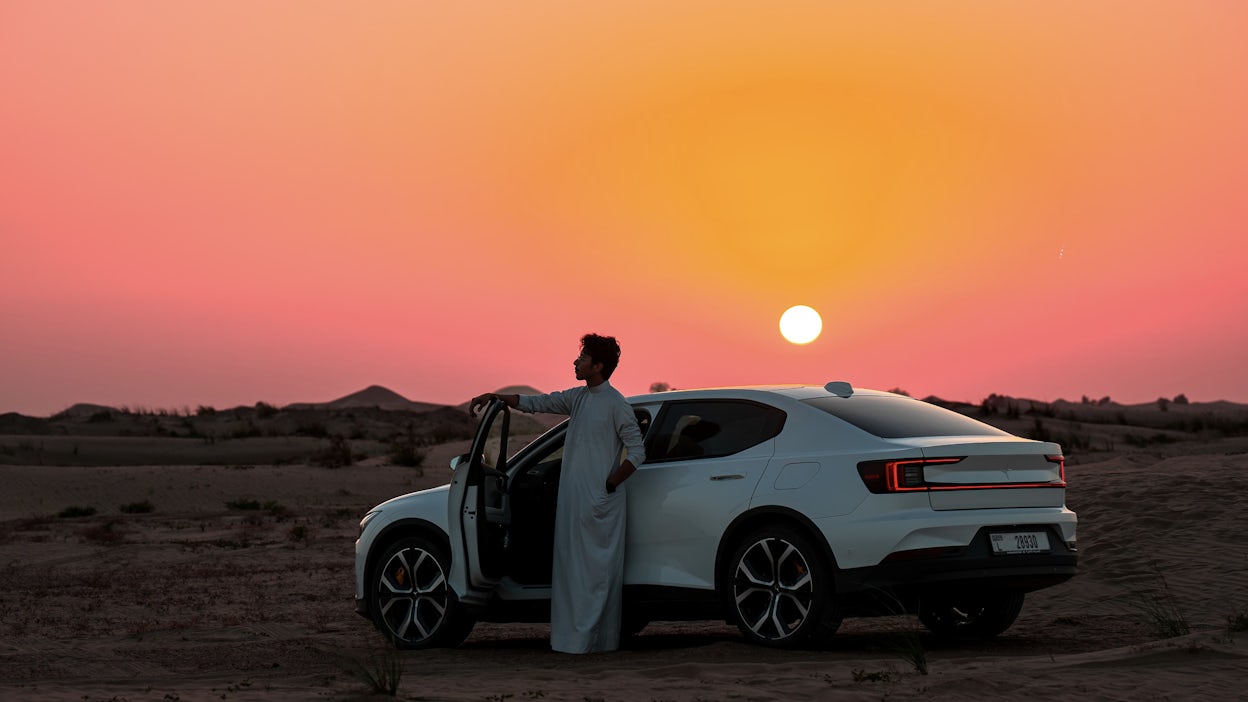 Man leaning on the door of Polestar 2 in the sunset.