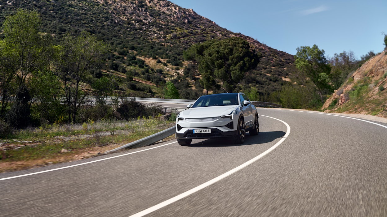 Polestar 3 in Snow color driving on a winding road in Spain, surrounded by trees and mountains