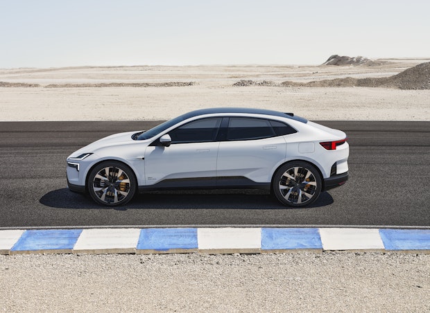 A white Polestar 4 electric SUV coupé is parked on a desert road next to a blue and white curb on a clear day.