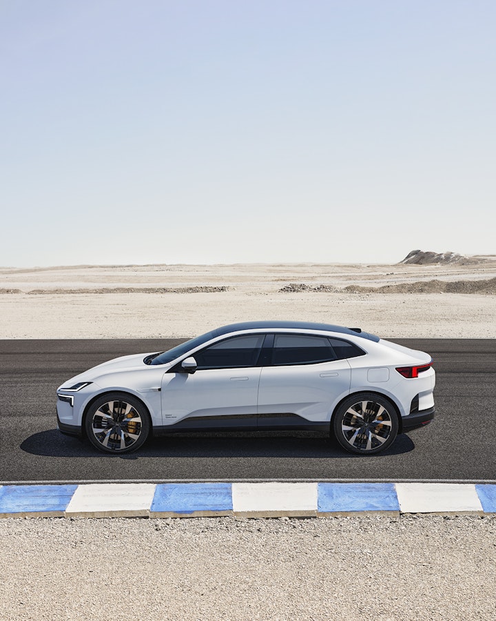 A white Polestar 4 electric SUV coupé is parked on a desert road next to a blue and white curb on a clear day.