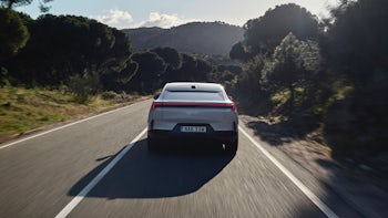 Media test driving a Polestar 4 in Spain on a straight asphalt road surrounded by forest