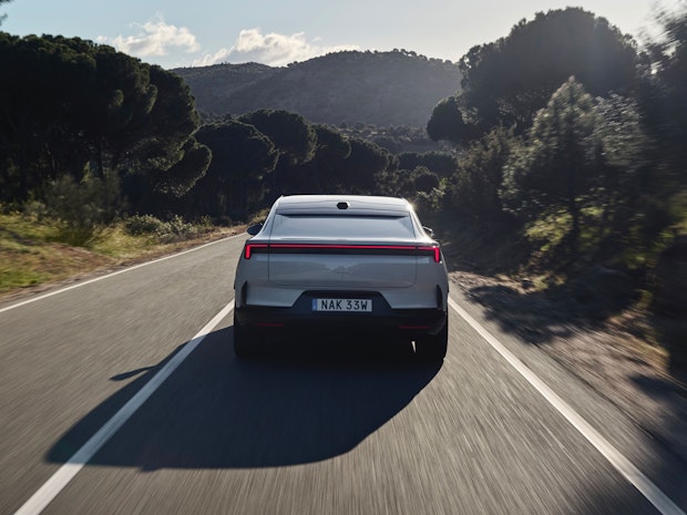 Media test driving a Polestar 4 in Spain on a straight asphalt road surrounded by forest