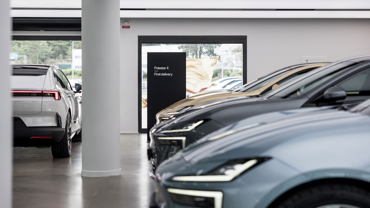 Three Polestar 4 cars in a row in the colors Electron, Storm, and Gold, in front of a sign that reads Polestar 4 First Delivery