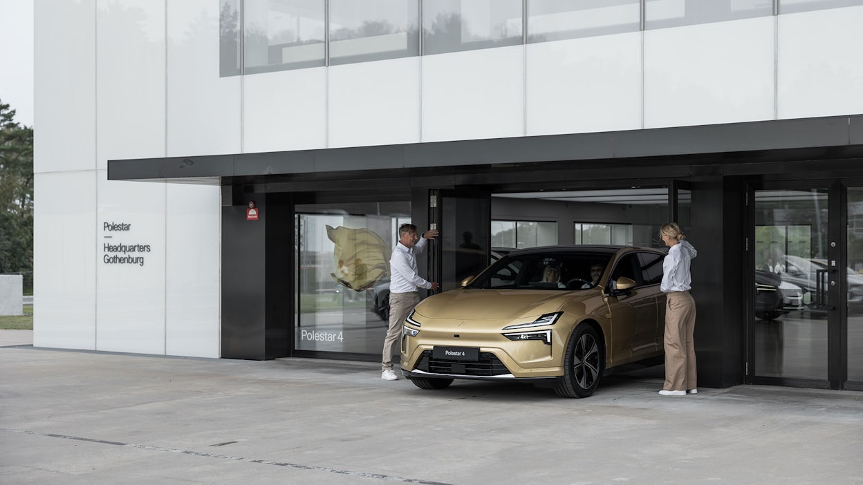 Two Polestar specialists opening glass doors for a Polestar 4 in Gold color