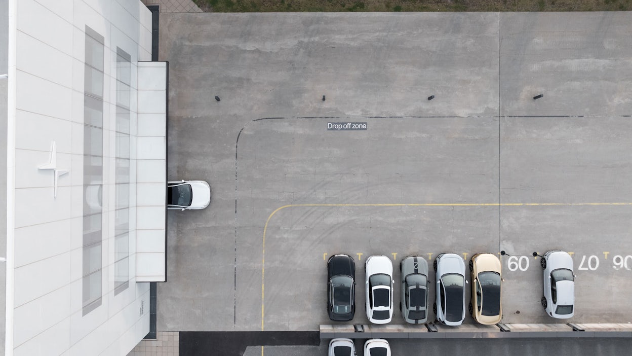 Aerial view of the parking lot at Polestar HQ, with a Polestar 4 about to drive out and several Polestar cars lined up in the parking lot