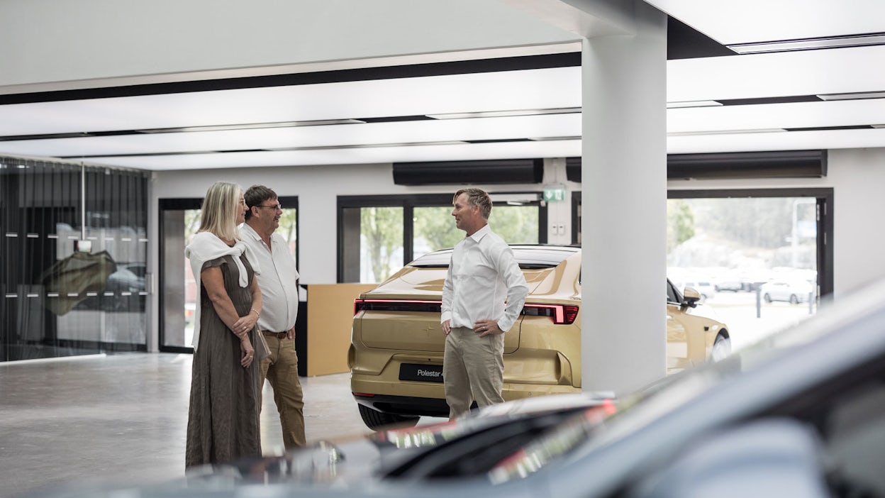 Ola Aldensjö talking with two customers in front of a Polestar 4 in Gold color