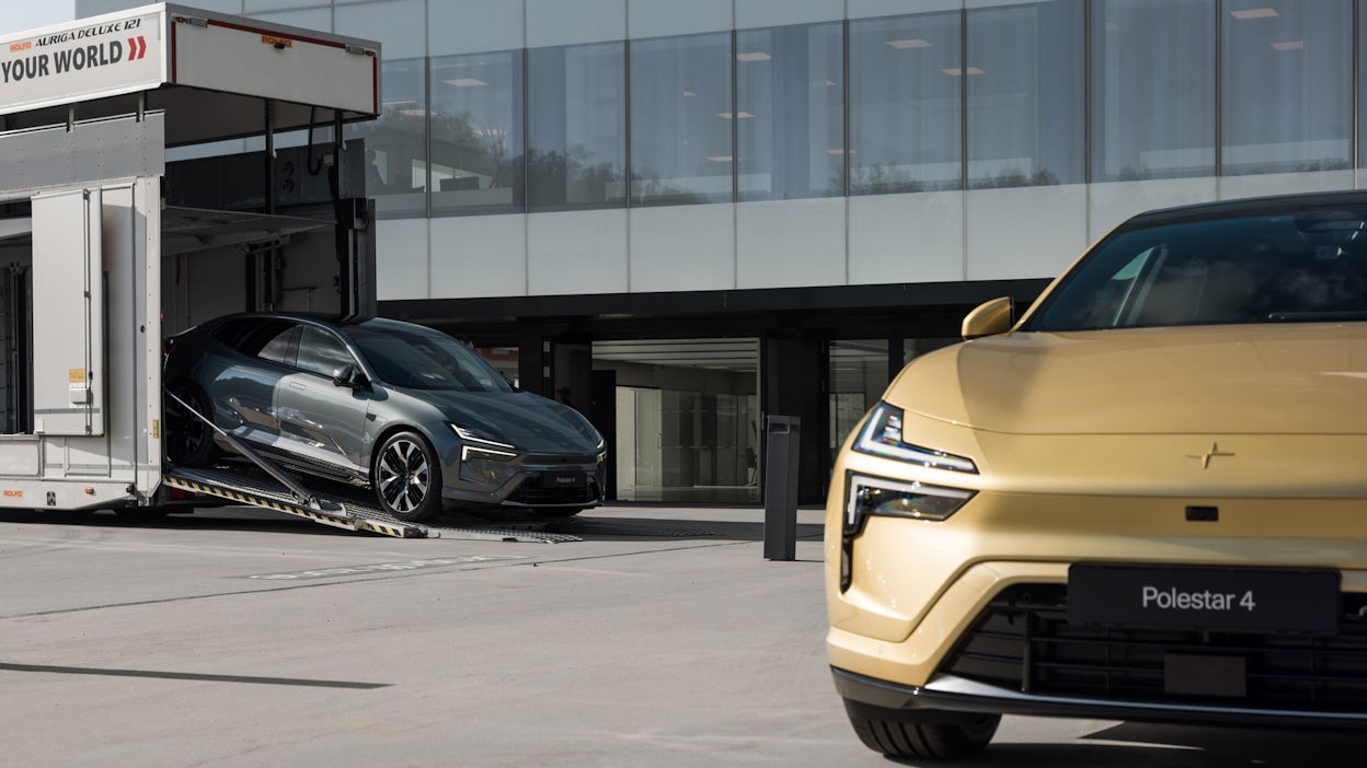 A partial view of a Polestar 4 front in Gold color with a Polestar 4 driving out of a truck in the background