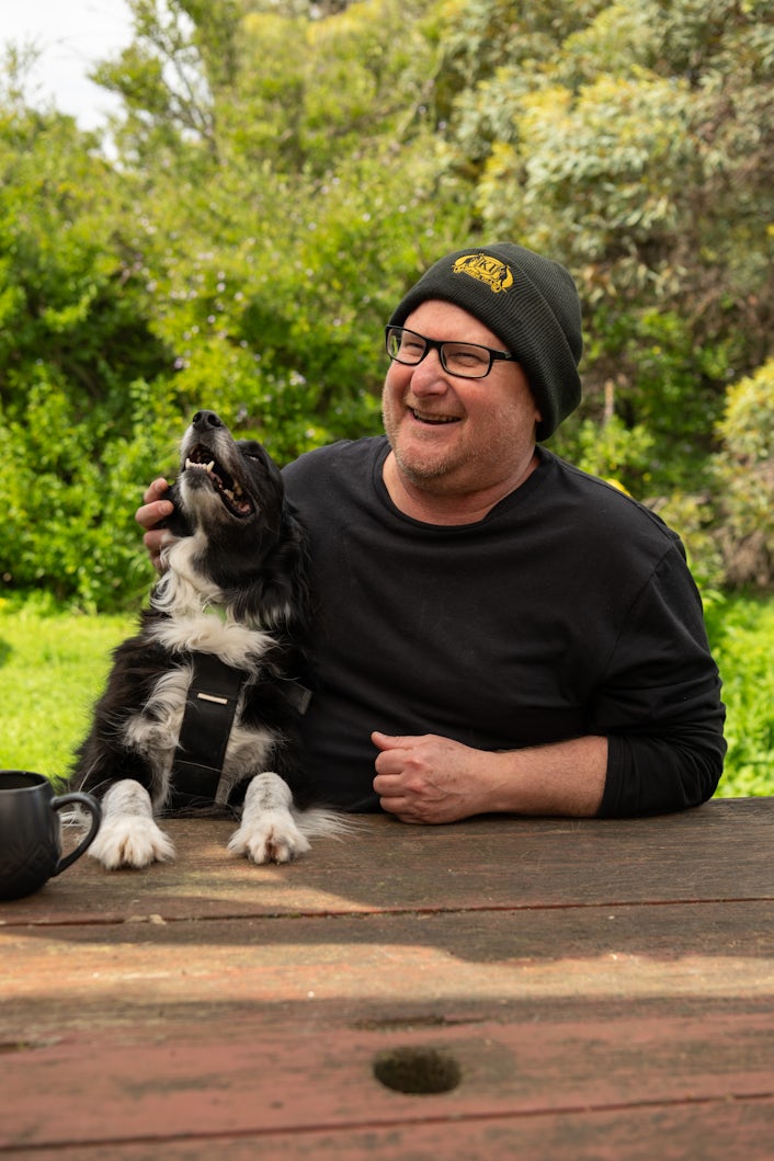 Stan and his pet dog sit at a table in his backyard on Kangaroo Island