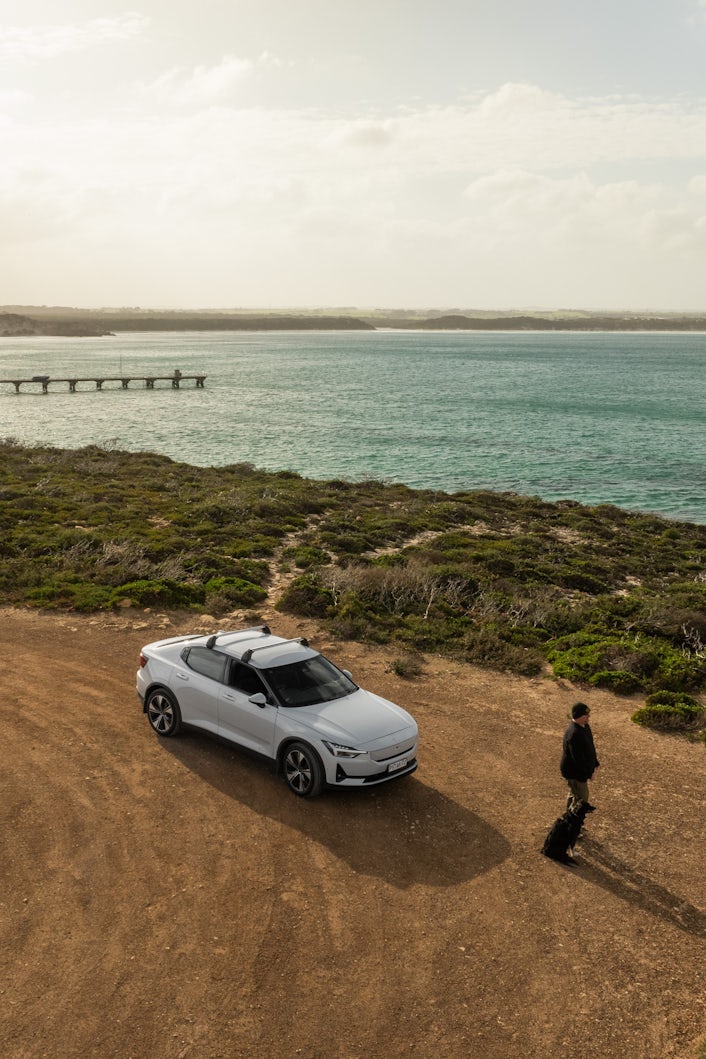 Stan and his pet dog Twiggy stand in front of Stan's Polestar 2, looking out to the ocean.