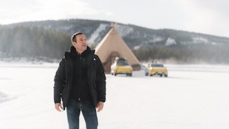 Man standing on frozen lake with cars and large tipi in background